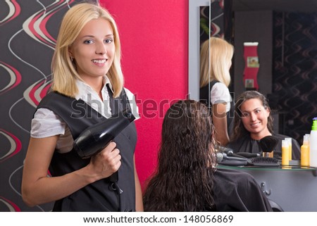 young beautiful hairdresser with hairdryer and smiling customer in beauty salon