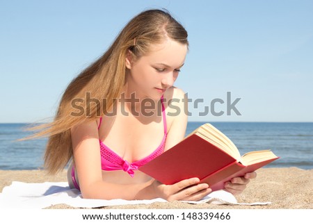 young attractive woman in pink bikini reading book on the beach