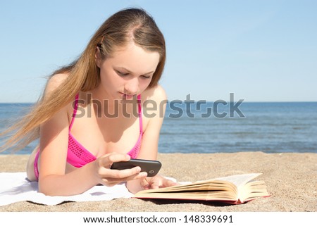 beautiful woman in pink bikini lying on the beach with mobile phone and book