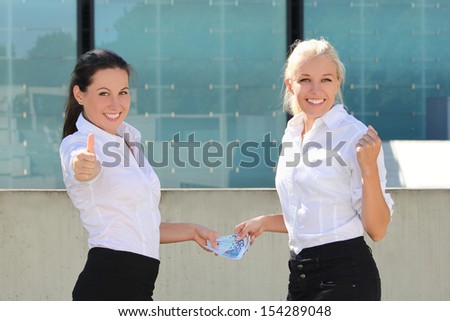 two business women thumbs up with euro banknotes over street background