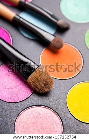 Make-up brushes and colorful eyeshadow palette over black background close up