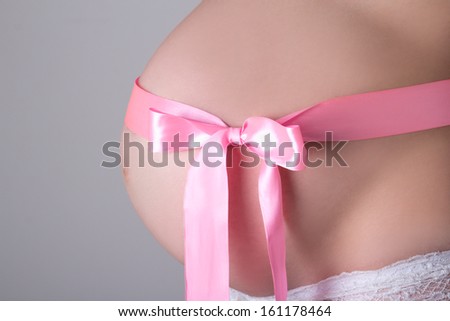 Close up image of pregnant woman tummy with pink ribbon over grey