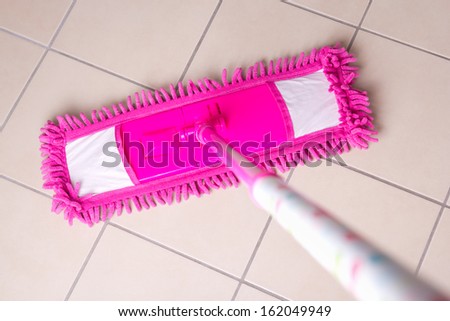 Pink mop cleaning light tile floor in bathroom