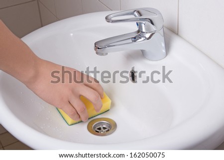 Male hand with yellow sponge cleaning white sink
