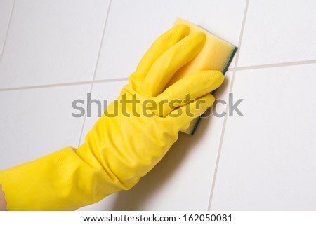 Hand in yellow glove cleaning tile wall