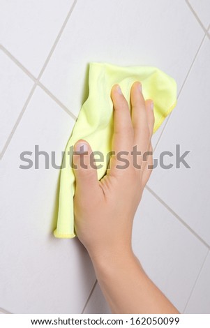 Hand with yellow rag cleaning tile wall
