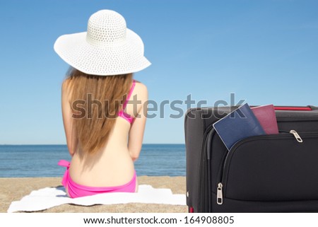 woman in hat sitting  and suitcase with passports on the beach