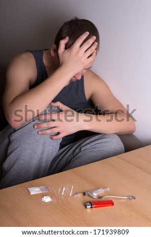 young depressed man with heroin addiction and drugs on the table