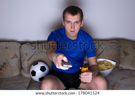 football supporter in uniform sitting on the sofa and changing channels with remote control