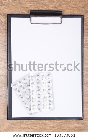 blank clipboard and pills on wooden table background