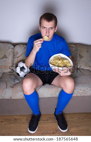 supporter in uniform watching football on tv at home and eating chips