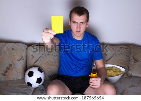 young man in uniform watching football on tv and showing yellow card