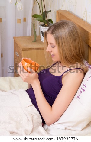 young attractive woman sitting in bed with mug of coffee or tea