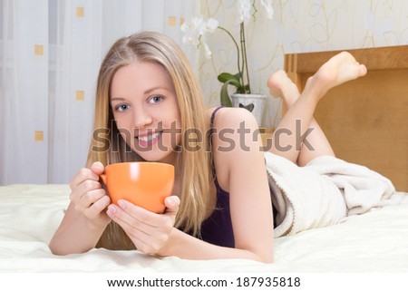 young beautiful woman lying on bed in bedroom with mug of coffee