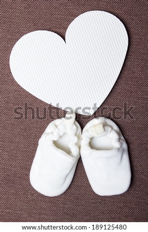 baby shoes and plastic heart over brown background