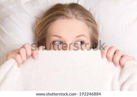 portrait of funny young beautiful woman lying in bed under blanket