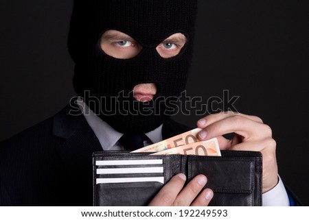 corruption concept - man in business suit and black mask holding leather purse with money