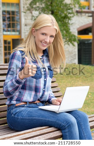 beautiful teenage girl sitting in park with laptop and thumbs up