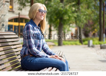 young attractive blond woman sitting on bench in park