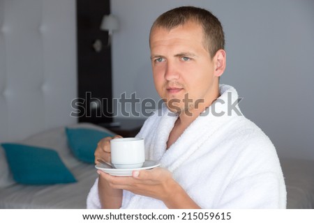 happy young man in bathrobe drinking coffee in hotel room