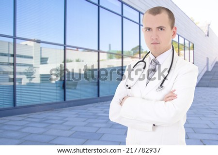 young male doctor standing on street against modern hospital building