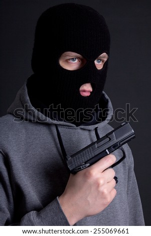 man criminal in black mask with gun over grey background