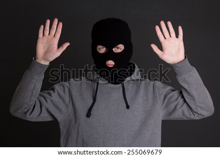 man in black mask holding hands up over grey background