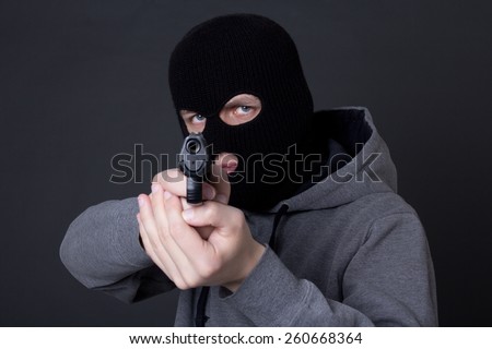masked man criminal aiming with gun over grey background