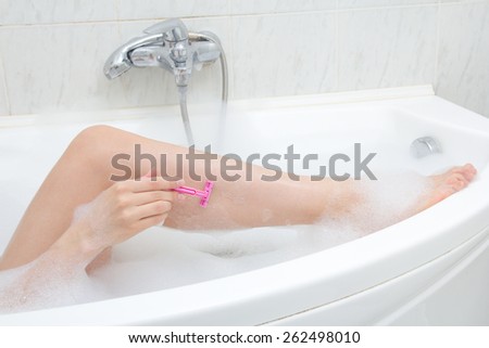 young woman shaving legs in bubble bath