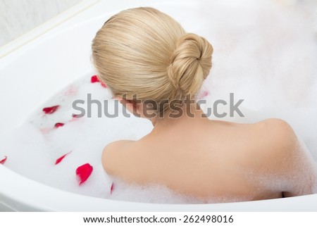 back view of woman relaxing in bubble bath with red flower petals