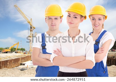 team work concept - two young women and man in blue builder \'s uniform at construction site
