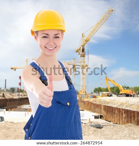beautiful woman builder in blue coveralls thumbs up at construction site