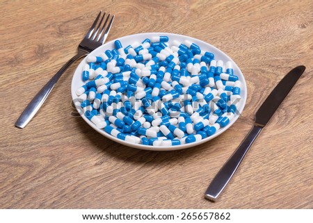 diet concept - blue pills in plate with knife and fork on wooden table