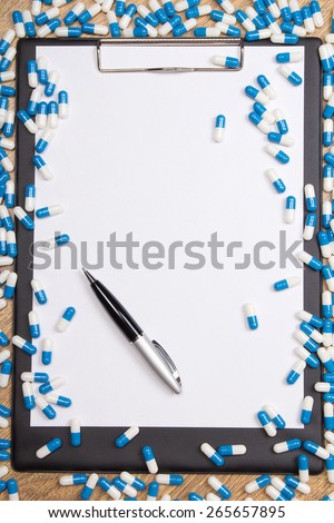 heal of blue pills, clipboard and pen on wooden table