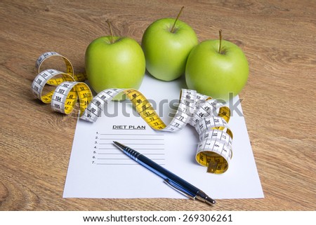 weightloss concept - close up of paper with diet plan, apples and measure tape on wooden table