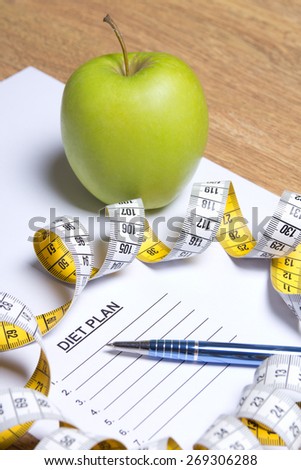 sheet of paper with diet plan, apple, pen and yellow measure tape