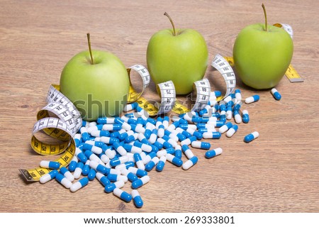 diet concept - apples, pills and measure tape on wooden table