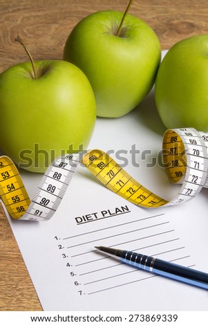 diet concept - paper with diet plan, apples and measure tape on wooden table