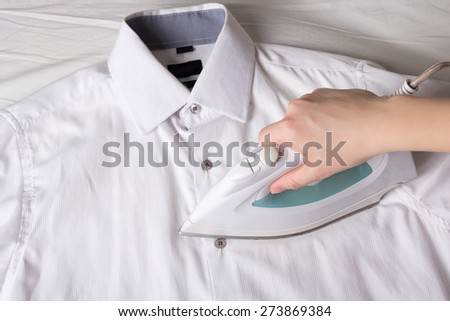 female hand with iron ironing white cotton shirt