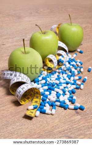 diet concept - green apples, pills and measure tape on wooden table