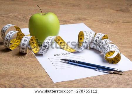 paper with diet plan, apple and measure tape on wooden table