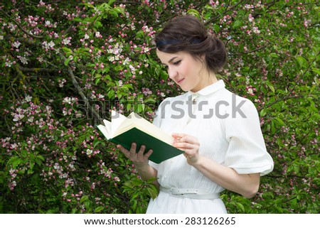portrait of young beautiful woman reading book in blooming spring garden