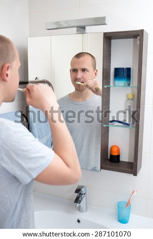 young handsome man brushing teeth and looking at mirror in bathroom