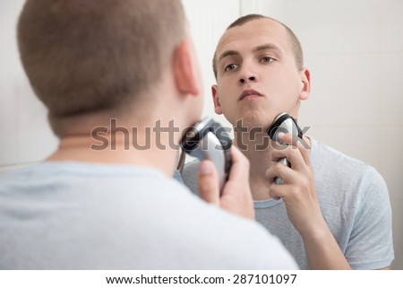 handsome man shaving with electric razor in bathroom