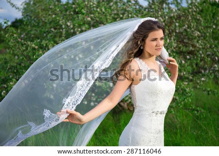 young beautiful bride with long veil in blooming summer garden