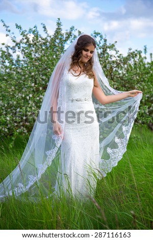 young beautiful bride with long veil walking in blooming summer garden