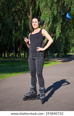 happy young brunette woman on roller skates listening music in summer park