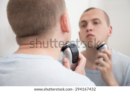 young handsome man in mirror shaving with electric shaver