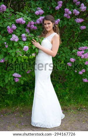young beautiful bride in wedding dress posing near blooming lilac tree