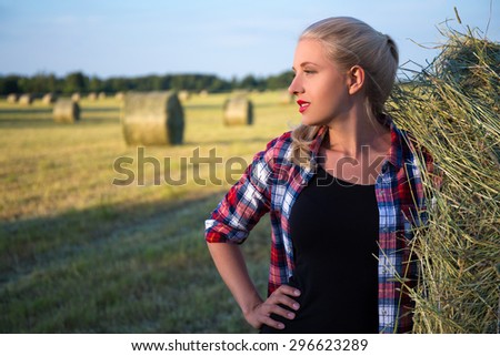 portrait of young beautiful blonde woman in field with haystacks